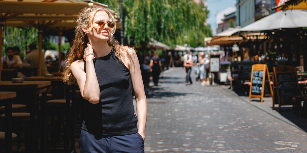 Dame steht in einem Marktplatz und trägt eine Sonnenbrille und ein Merino-Oberteil.