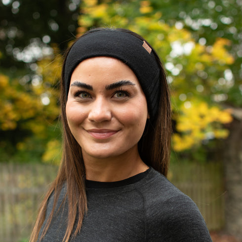 Eine Frau mit einem schwarzen Stirnband aus 100% Merinowolle in der Natur.