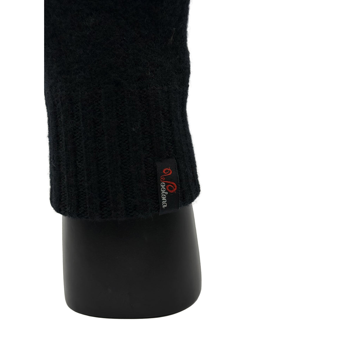 Aus der nähe eine Hand die ein Handschuh aus Merinowolle in Schwarz trägt und das Woolona Logo zeigt