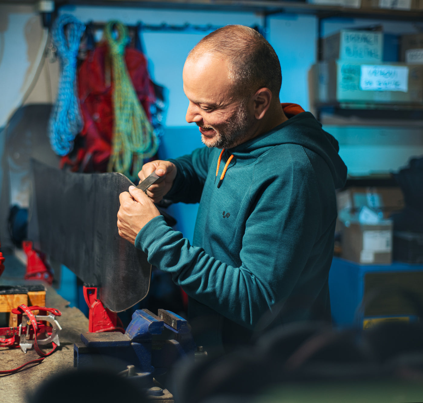 Ein Mann bearbeitet an einer Werkbank an einerm Snowboard und trägt einen Merino Hoodie