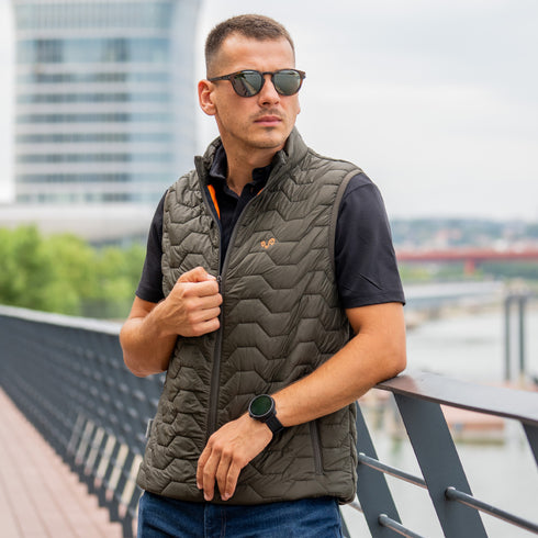 Mann steht auf einer Brücke und trägt eine grüne Outdoor-Weste mit Wolle als Innenfutter