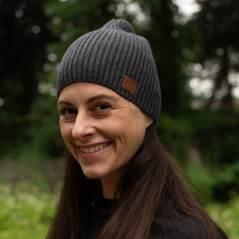 Eine Dame mit einer anthrazit farbenen Mütze aus Merinowolle mit einem Woolona Logo.