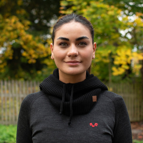 Eine Frau mit einem Merino Kapuzenschal in der Farbe schwarz mit braunen Logo.