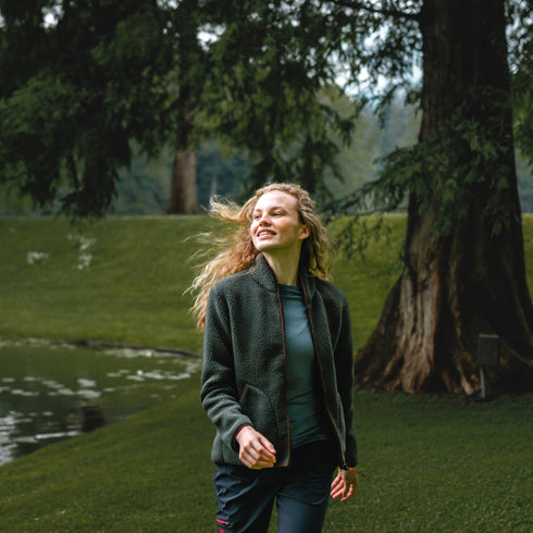 Wanderin am See lächelt und läuft mit einer grünen Sherpajacke mit Merino umher.