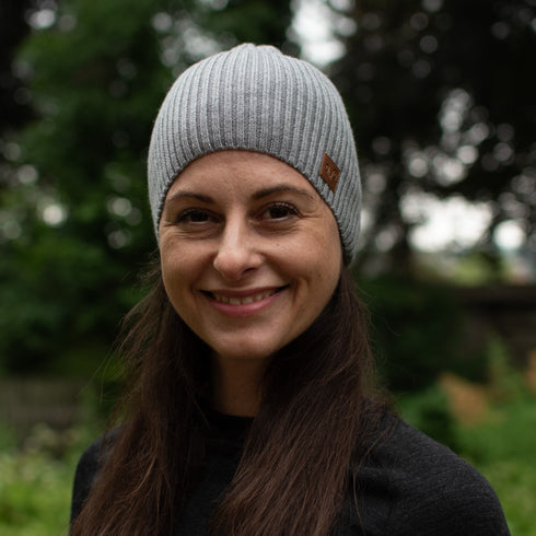 Eine Dame mit einer grauen Merinomütze mit braunem Logo von Woolona.