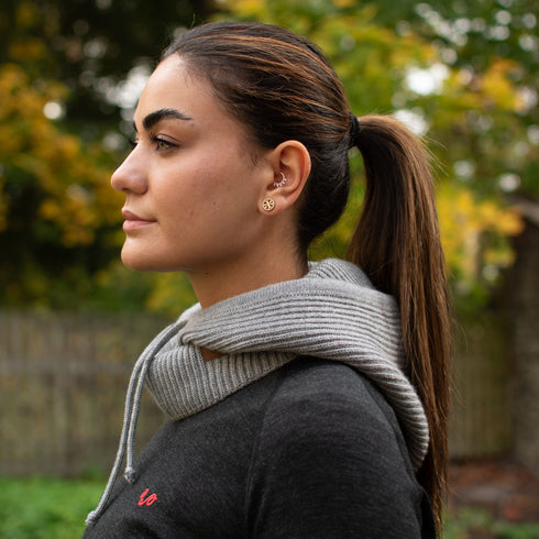 Frau mit braunen Haaren von der Seite, trägt einen Kapuzenschal aus Merinowolle in de Farbe grau.