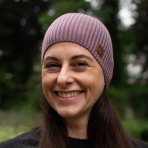 Lachende Frau mit einer violett farbenen Herbst- und Wintermütze aus Merinowolle.
