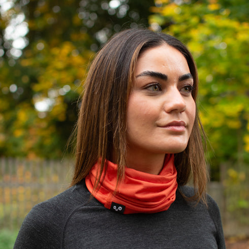 Die Wanderin trägt einen Orange farbenen Nackenwärmer aus 100% Merinowolle.
