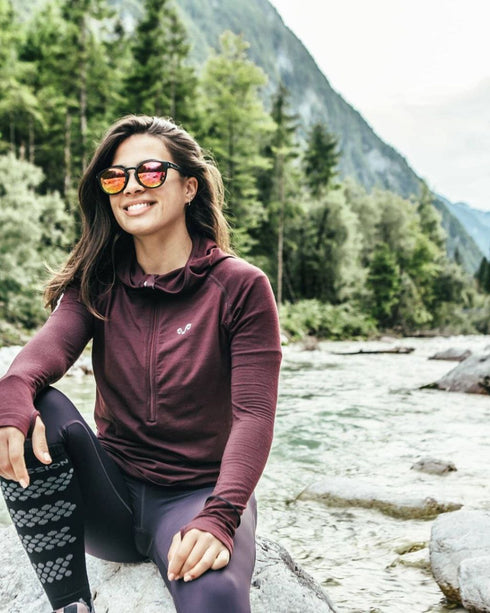 Frau mit Merino Langarmshirt mit Reißverschluss in Pflaume am Fluss in den Bergen