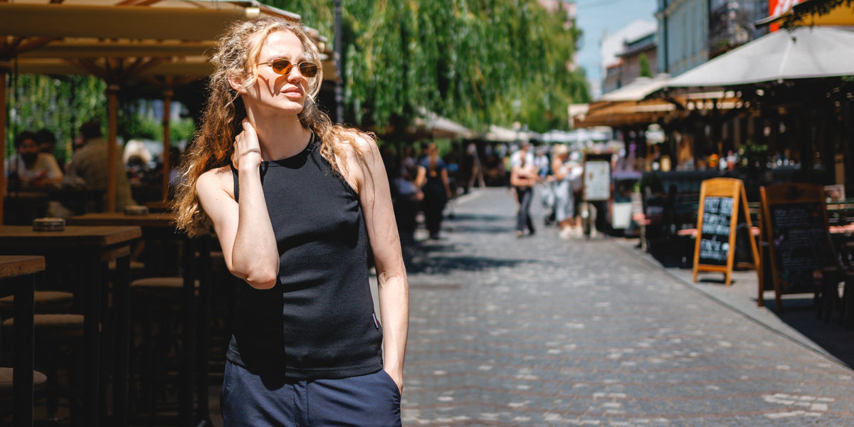 Dame steht in einem Marktplatz und trägt eine Sonnenbrille und ein schwarzes Merino-Tanktop.