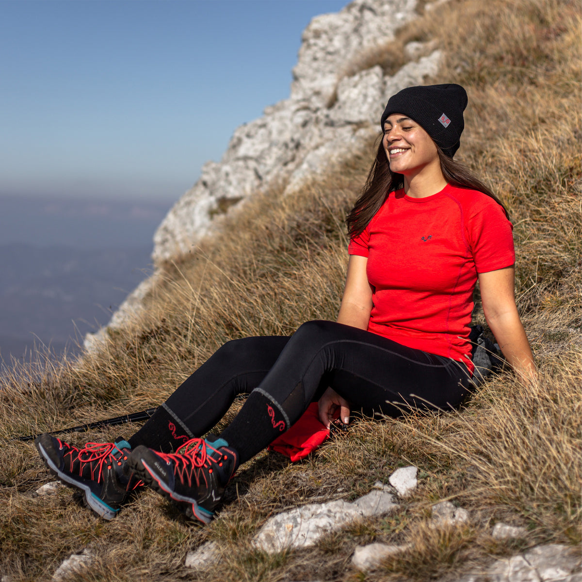 Eine Frau sitzt auf einer Wiese und trägt ein Rotes Merino-T-Shirt