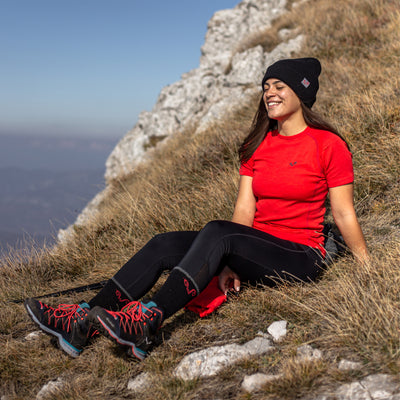 Eine Frau sitzt auf einer Wiese und trägt ein Rotes Merino-T-Shirt