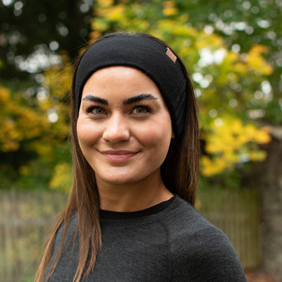 Eine Frau mit einem schwarzen Stirnband aus 100% Merinowolle in der Natur.