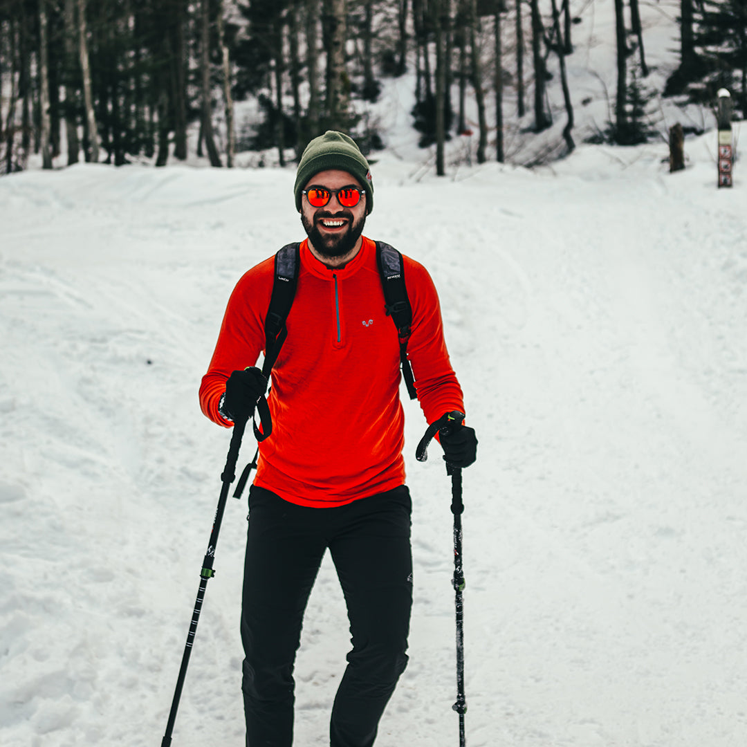 Skifahrer trägt Merino-Langarmshirt von Woolona in der Farbe Orange, lächelt und fährt Ski.