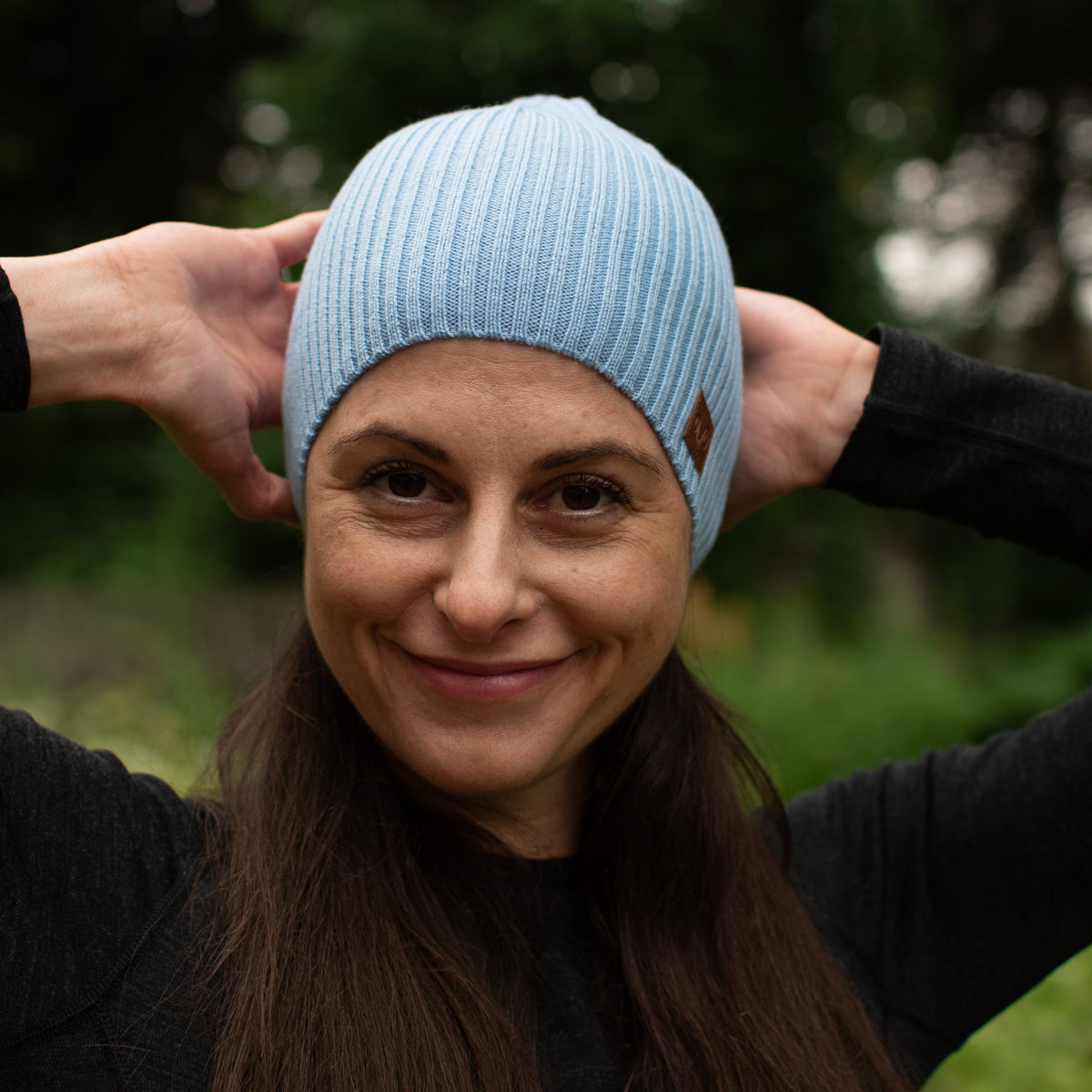 Frau mit einer hellblauen Merinomütze in der Natur. 