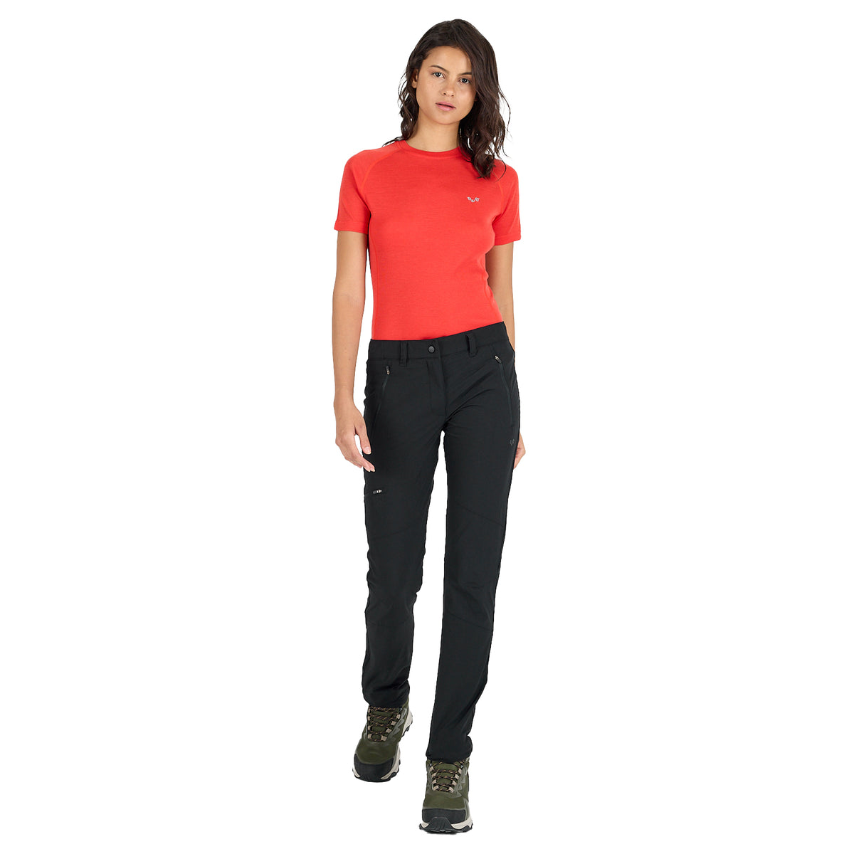 Frau mit schwarzer Merino Outdoorhose mit Reißverschlüssen und einem orangen Merino Tshirt.